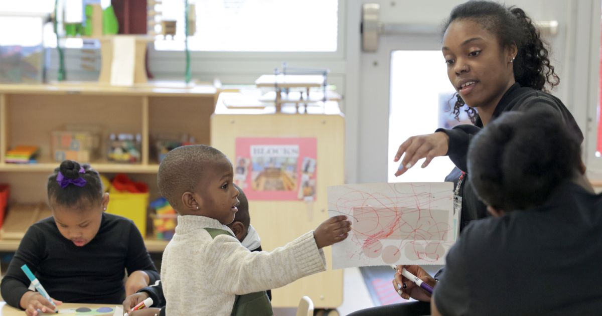 Preschool children sitting in classroom with an educator talking to them.