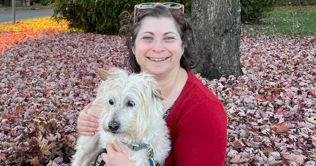 Stacie sitting in the fallen leaves with her dog Neville