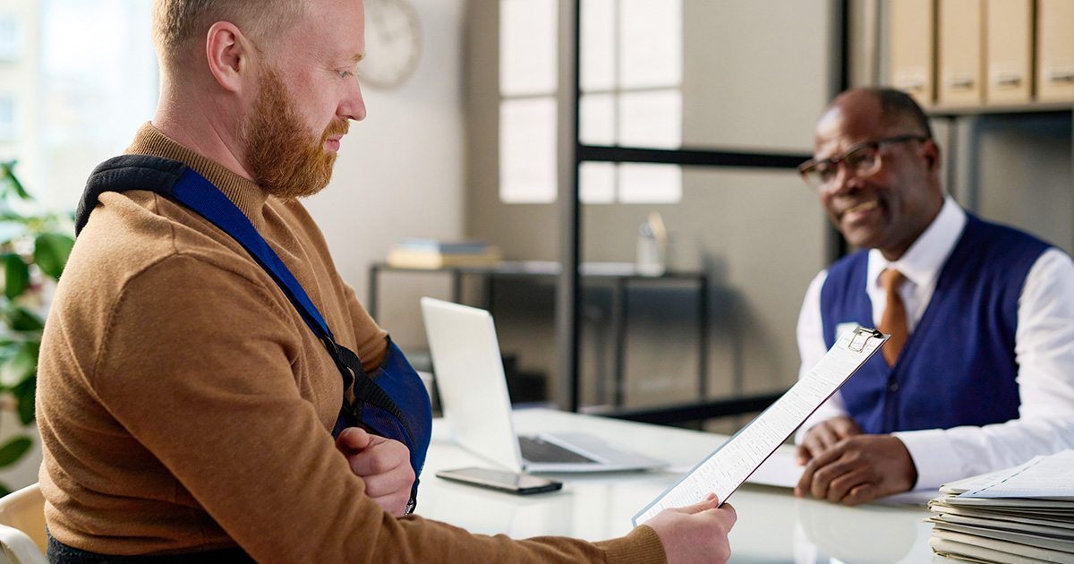 A patient in an arm sling consults with a professional behind a desk