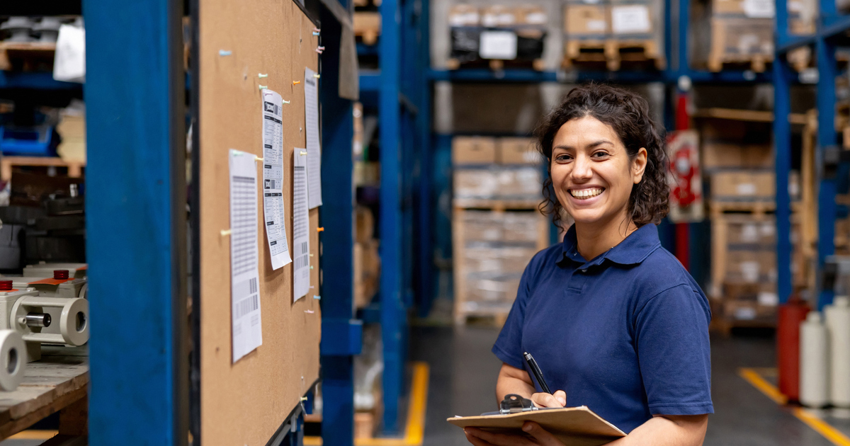 Warehouse employee looking at her shifts on a bulletin board and smiling stock photo