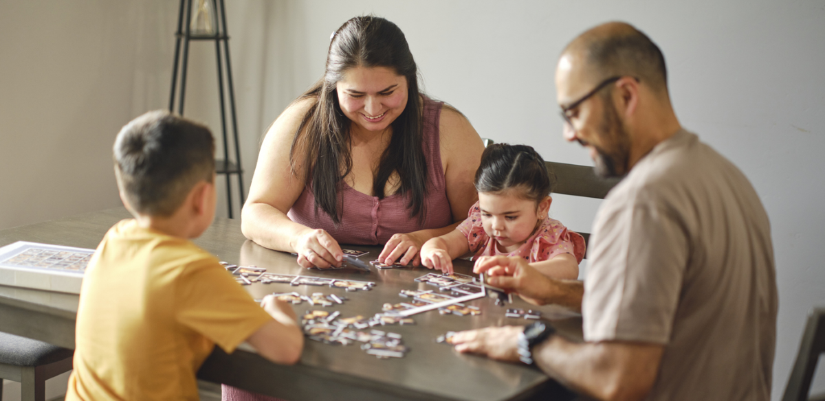 A Hispanic family in their home, doing a jigsaw puzzle together.