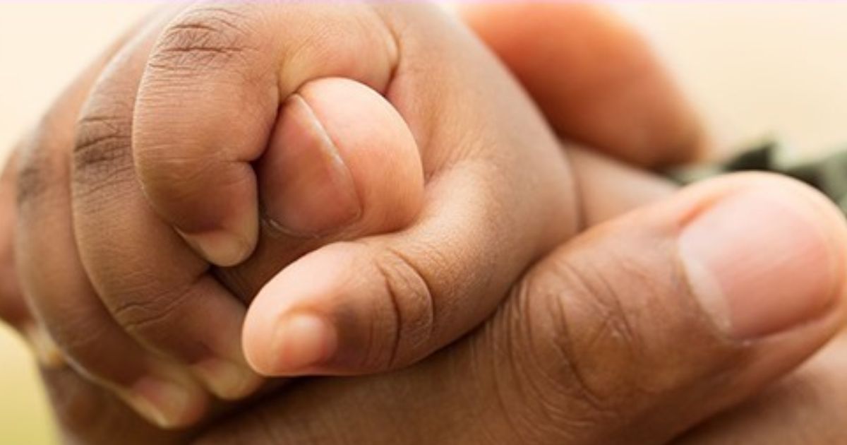 A child's hands grips an adult's hand.